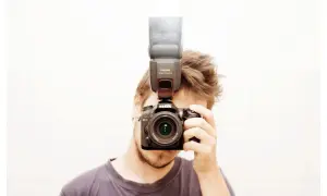 Mężczyzna z aparatem Nikon i lampą błyskową na gorącej stopce. Pokazuje, jak używać lampy błyskowej do lepszego oświetlenia.