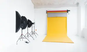 Studio fotograficzne z żółtym tłem do zdjęć, lampami i parasolami.