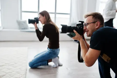 Dwóch fotografów, mężczyzna i kobieta, klęczy i robi zdjęcia. To inspiracja, jak zostać fotografem.