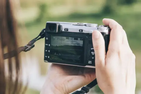 Dłonie trzymają aparat, który może być dobrym aparatem fotograficznym do 500 zł. Na ekranie widać krajobraz.