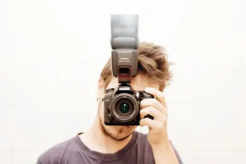 Mężczyzna z aparatem Nikon i lampą błyskową na gorącej stopce. Pokazuje, jak używać lampy błyskowej do lepszego oświetlenia.