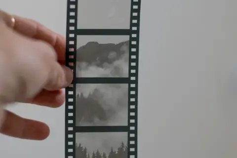 Dłoń trzyma kadr z taśmy filmowej, ukazujący mgliste góry i lasy.