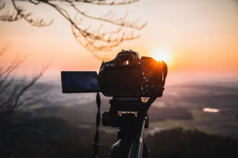 Aparat fotograficzny na statywie na tle zachodzącego słońca.