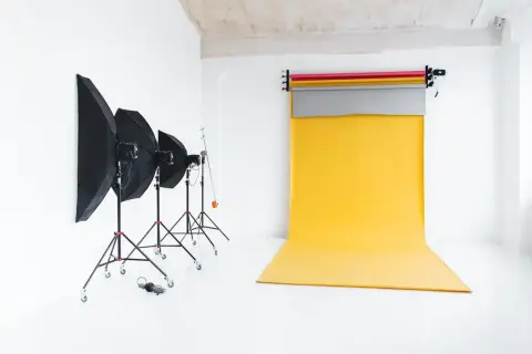 Studio fotograficzne z żółtym tłem do zdjęć, lampami i parasolami.