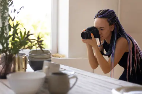 Kobieta z kolorowymi warkoczami robi zdjęcia ceramicznych naczyń. To przykład, jak wyglądają zdjęcia stockowe co to.
