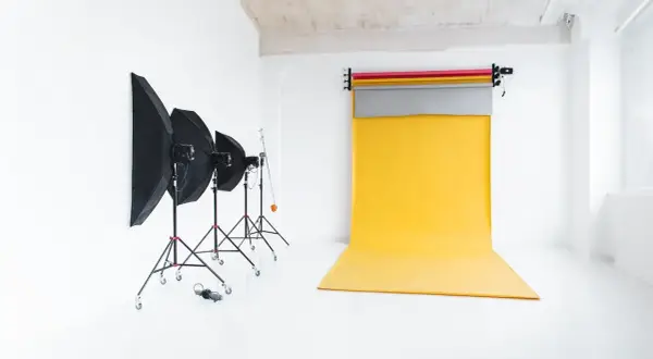 Studio fotograficzne z żółtym tłem do zdjęć, lampami i parasolami.