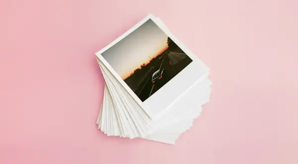 Stos odbitek zdjęć z podróży, na górze zdjęcie samochodu na autostradzie o zachodzie słońca. Zastanawiasz się, ile kosztuje wydrukowanie zdjęcia u fotografa?