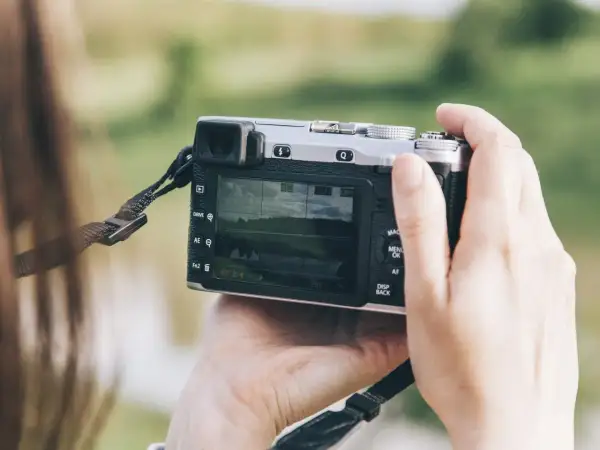 Dłonie trzymają aparat, który może być dobrym aparatem fotograficznym do 500 zł. Na ekranie widać krajobraz.